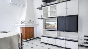 Una habitación con una mesa de comedor, un televisor integrado, un armario con cajones y suelo de baldosas.