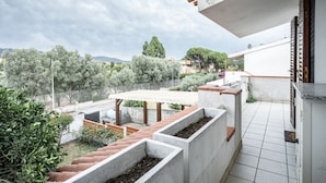 Un balcón con vista a un jardín, suelo de baldosas y una jardinera de hormigón.