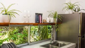 A modern kitchen with a stainless steel refrigerator, a sink, and a window overlooking a lush garden.