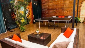 A room with a ping pong table, two sofas with orange cushions, a coffee table, and a mural with tropical and animal motifs.