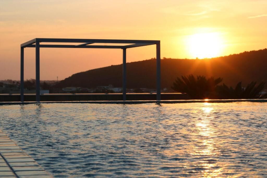 A swimming pool with a metal structure in the center, surrounded by water reflecting the sunset.