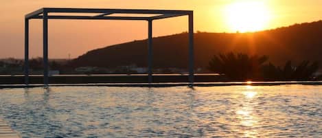 A swimming pool with a metal structure in the center, surrounded by water reflecting the sunset.