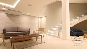 A modern living room with a sofa, chair, coffee table, and staircase. - Hihome - Royale (São Bento Cabo Frio)