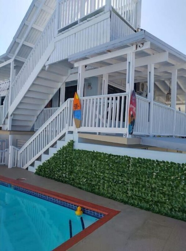 A white building with a swimming pool and a covered area with stairs.