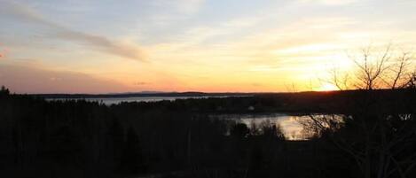 Un coucher de soleil sur un lac, avec une rive bordée d’une forêt.