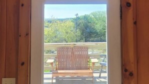 A wooden-framed door leading to an outdoor deck with a wooden chair and two small tables.