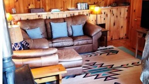 A cozy cabin interior with a leather sofa, a wooden table, and a patterned rug.