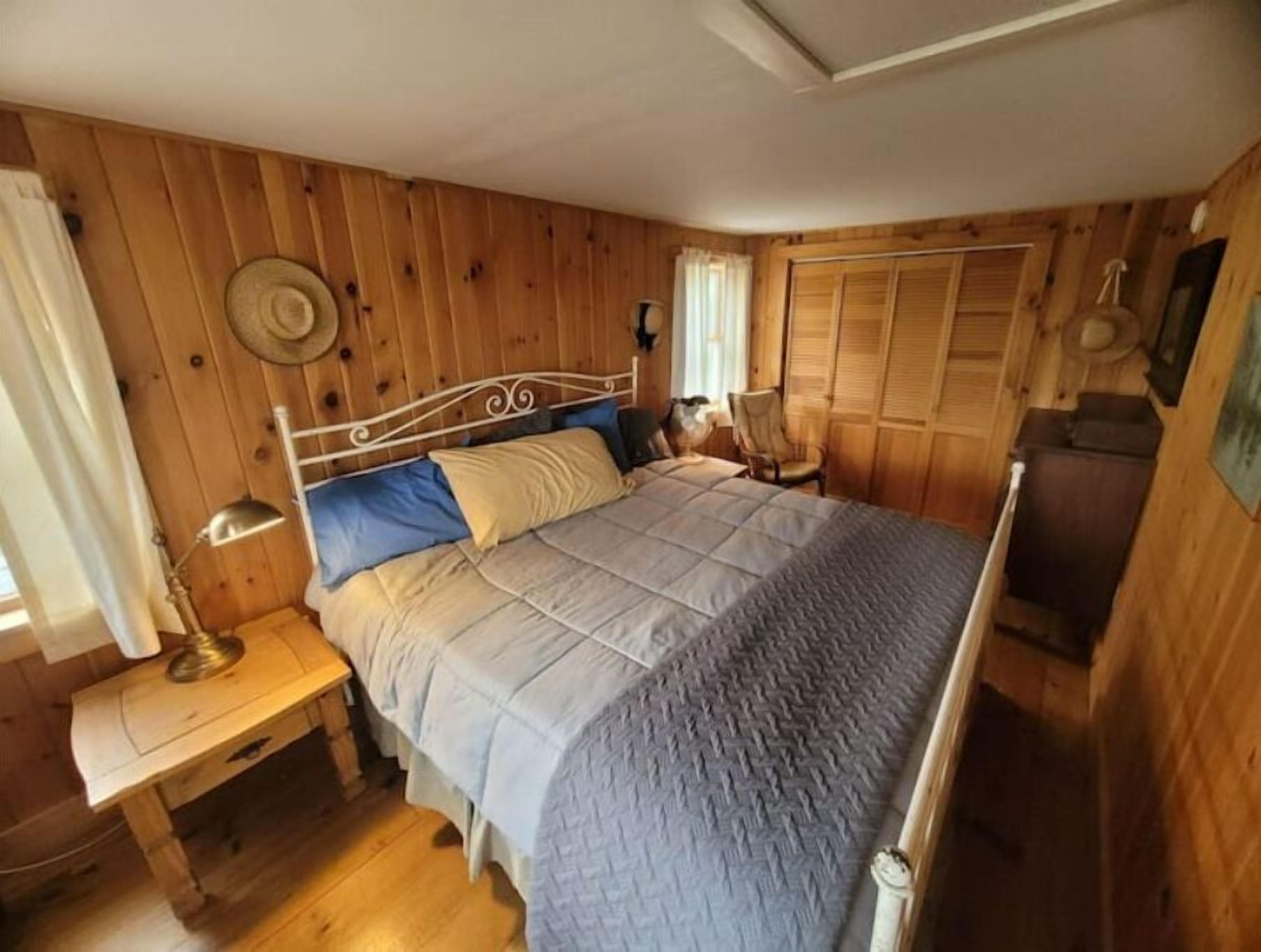 Ein Schlafzimmer mit Holzwandverkleidung, einem Bett, einem Nachttisch, einer Lampe, einem Sessel und einem Kleiderschrank.