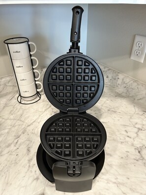 En vaffeljern på en marmorplade med en kaffemaskine ved siden af.