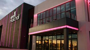 Een modern gebouw met een opvallend bord waarop 'Vibrant Music Hall' staat, grote glasramen en een plat dak.