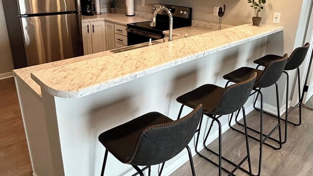 Een moderne keuken met een centraal eiland, barstoelen, roestvrijstalen apparatuur en hanglampen.