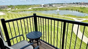 Een balkon met uitzicht op een meer, een golfbaan en gebouwen in de verte.