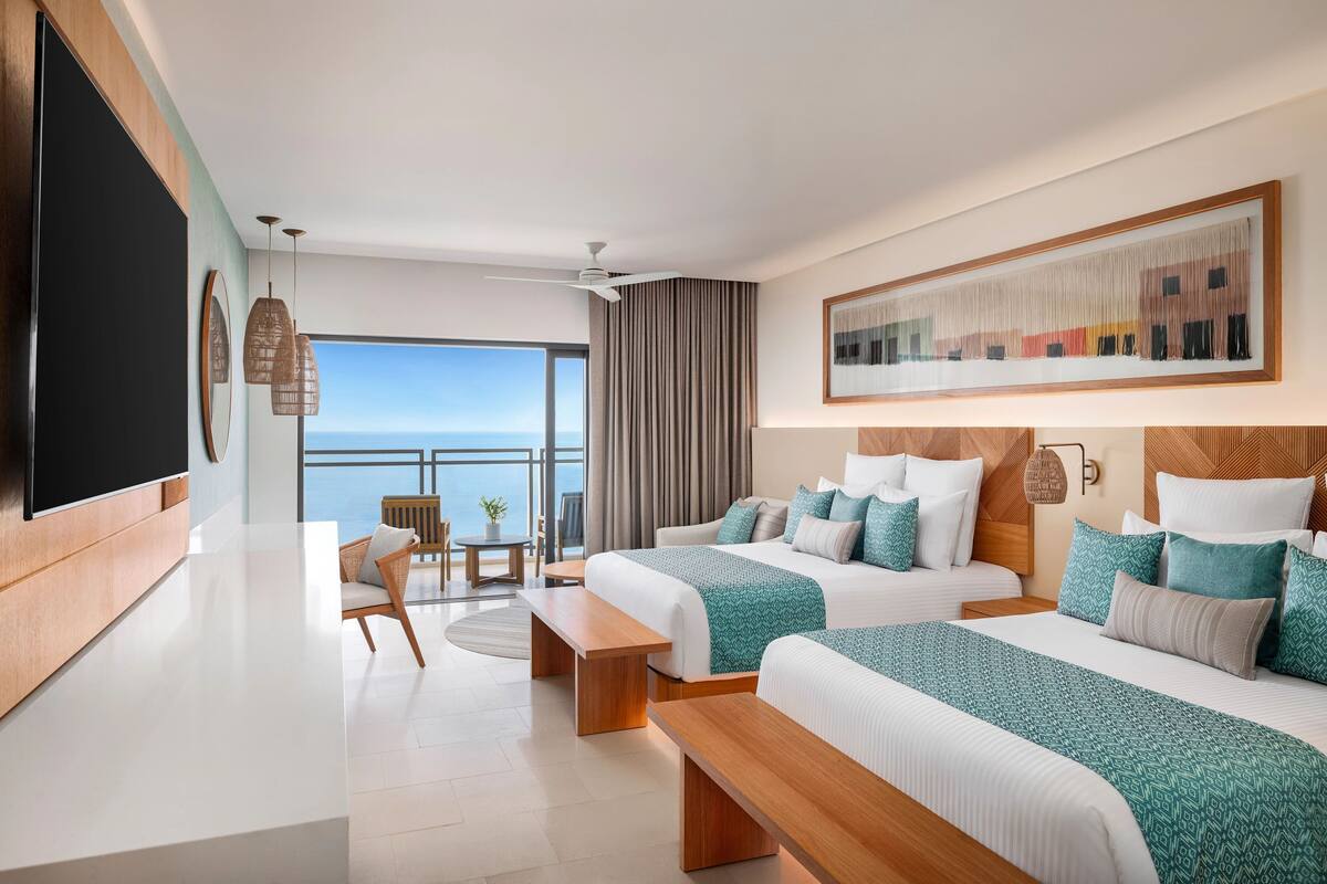 Une chambre d’hôtel moderne avec deux lits, une grande télévision, un balcon avec vue et un coin repas.