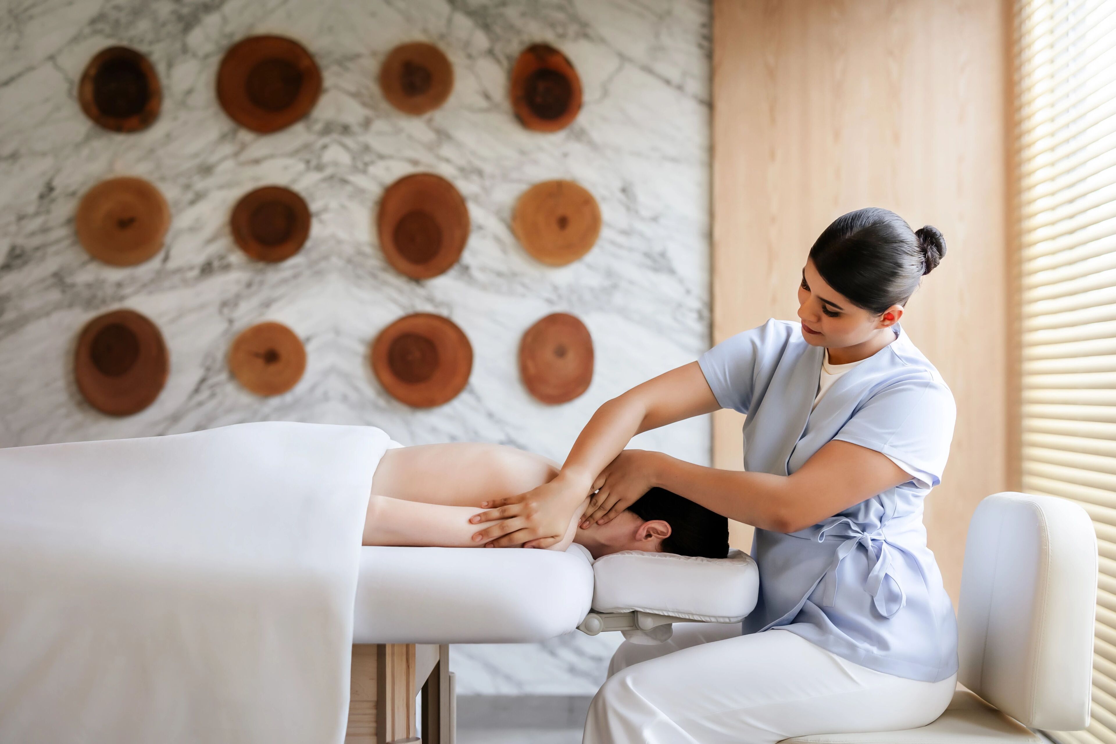 Eine Massageanwendung in einer Wellnessumgebung mit Marmorwand und Holzelementen.