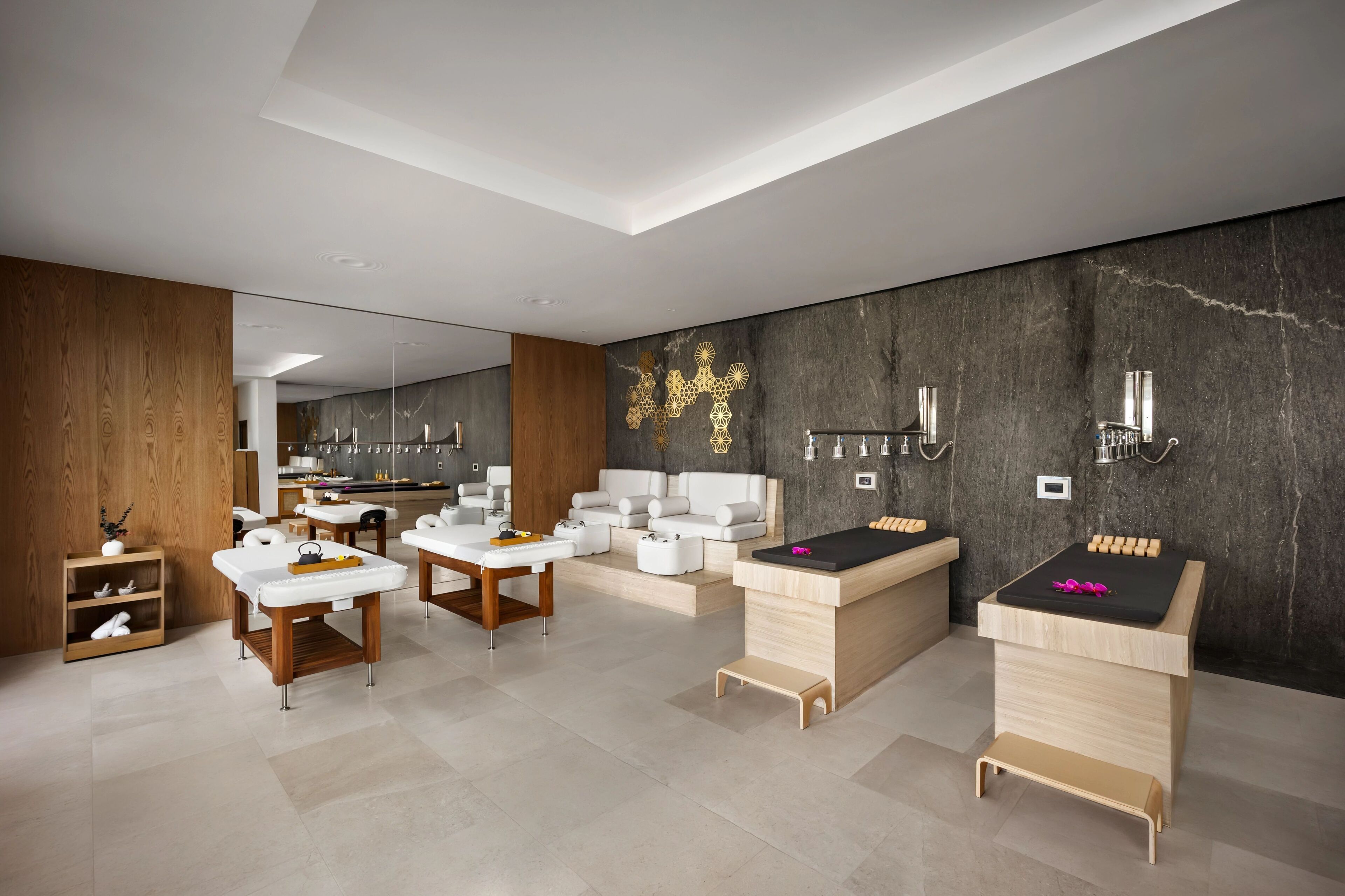 A modern spa with wooden and white furniture, a massage table, and a wall with a geometric design.