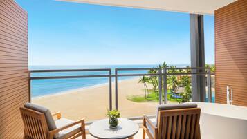 A balcony with a view of a beach, two wooden chairs, a small table, and a potted plant.