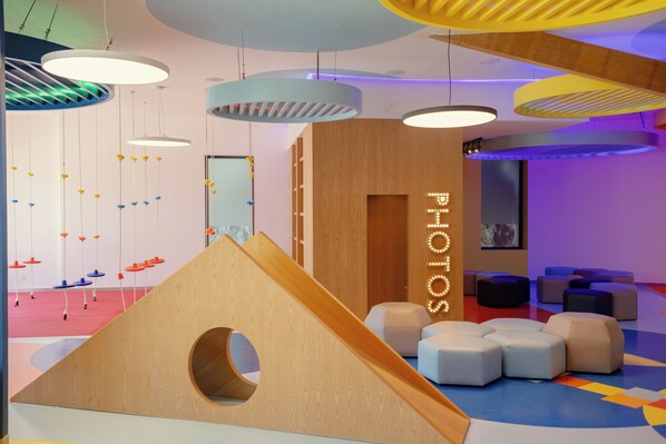 Un interior moderno con una estructura de juego de madera, luces colgantes y zonas de estar coloridas.
