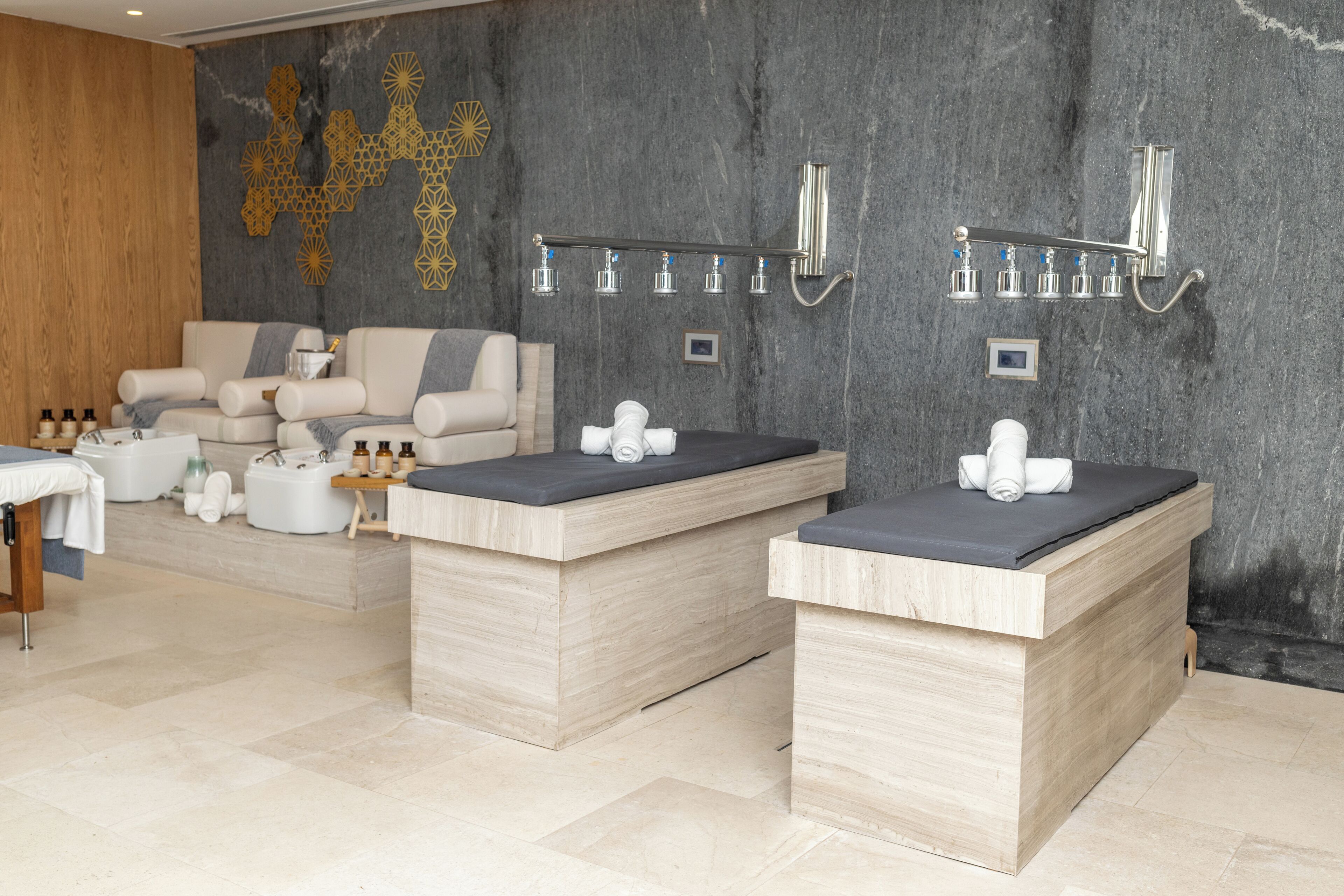 Un área de spa con dos camillas de madera, un banco de madera y una lámpara fijada a la pared.