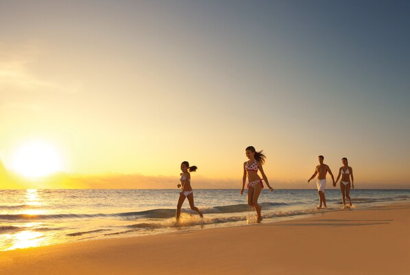 Escena de playa con gente caminando por la orilla al atardecer.