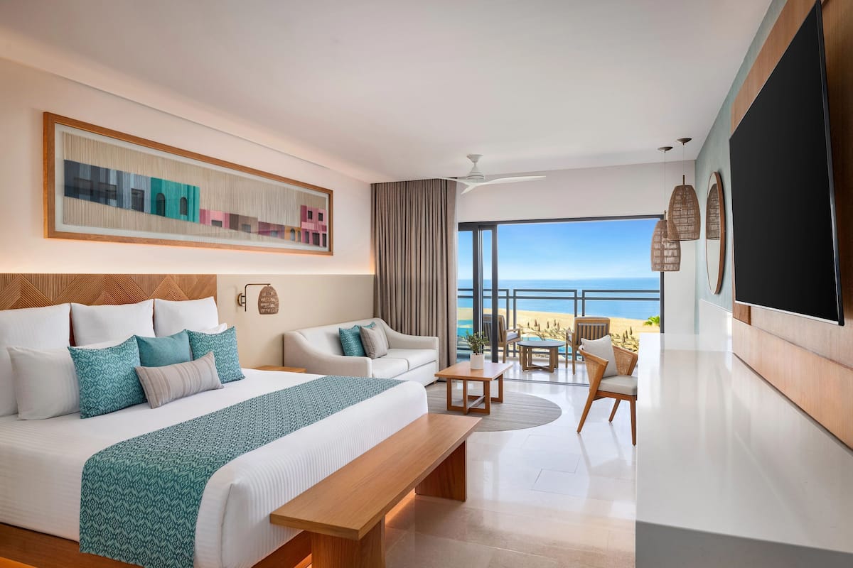 Une chambre d’hôtel moderne dotée d’un grand lit, d’un canapé, d’un coin repas et d’un balcon offrant une vue sur la plage.
