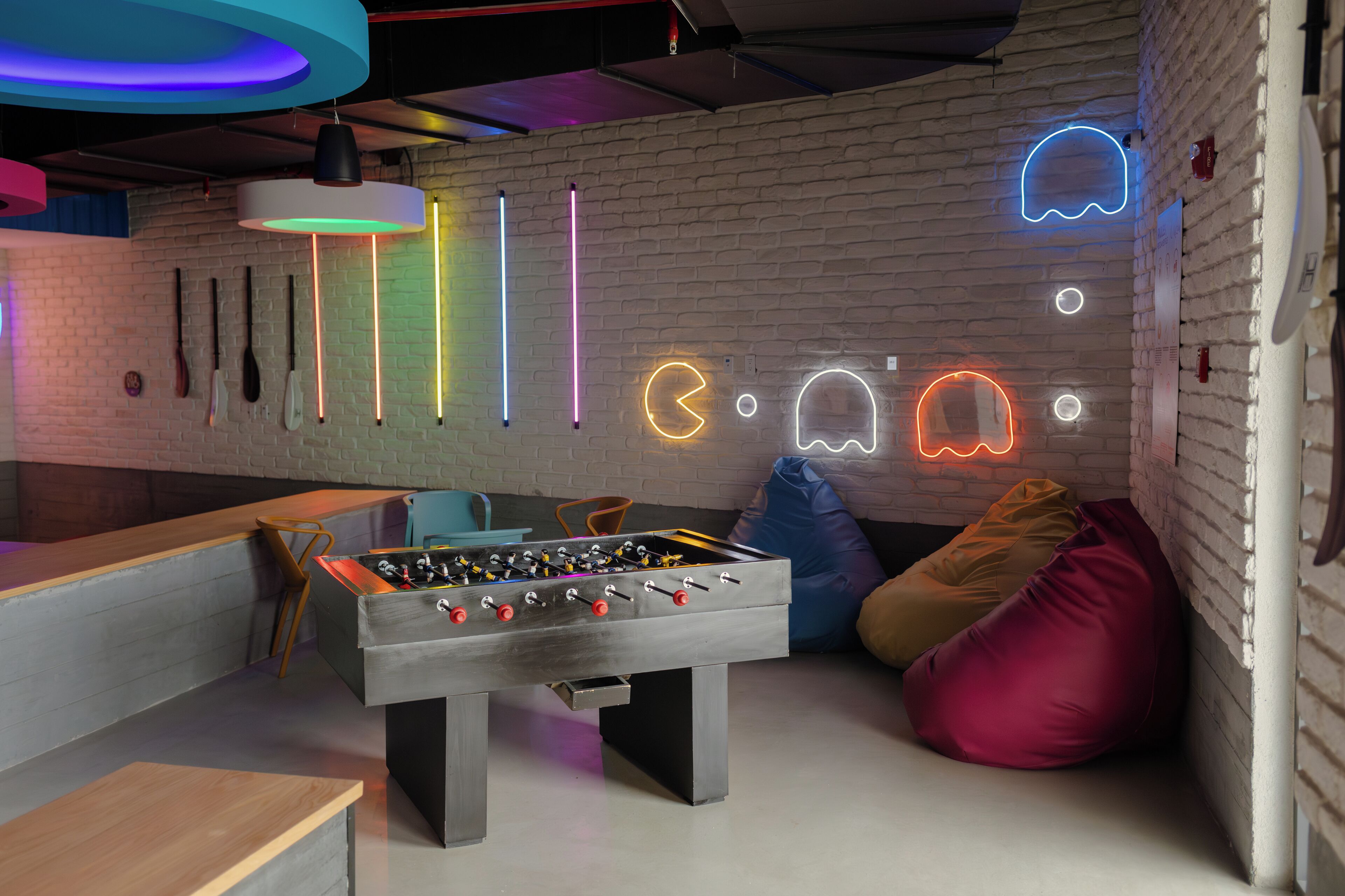 A modern indoor space with a foosball table, neon wall art, and a brick wall.