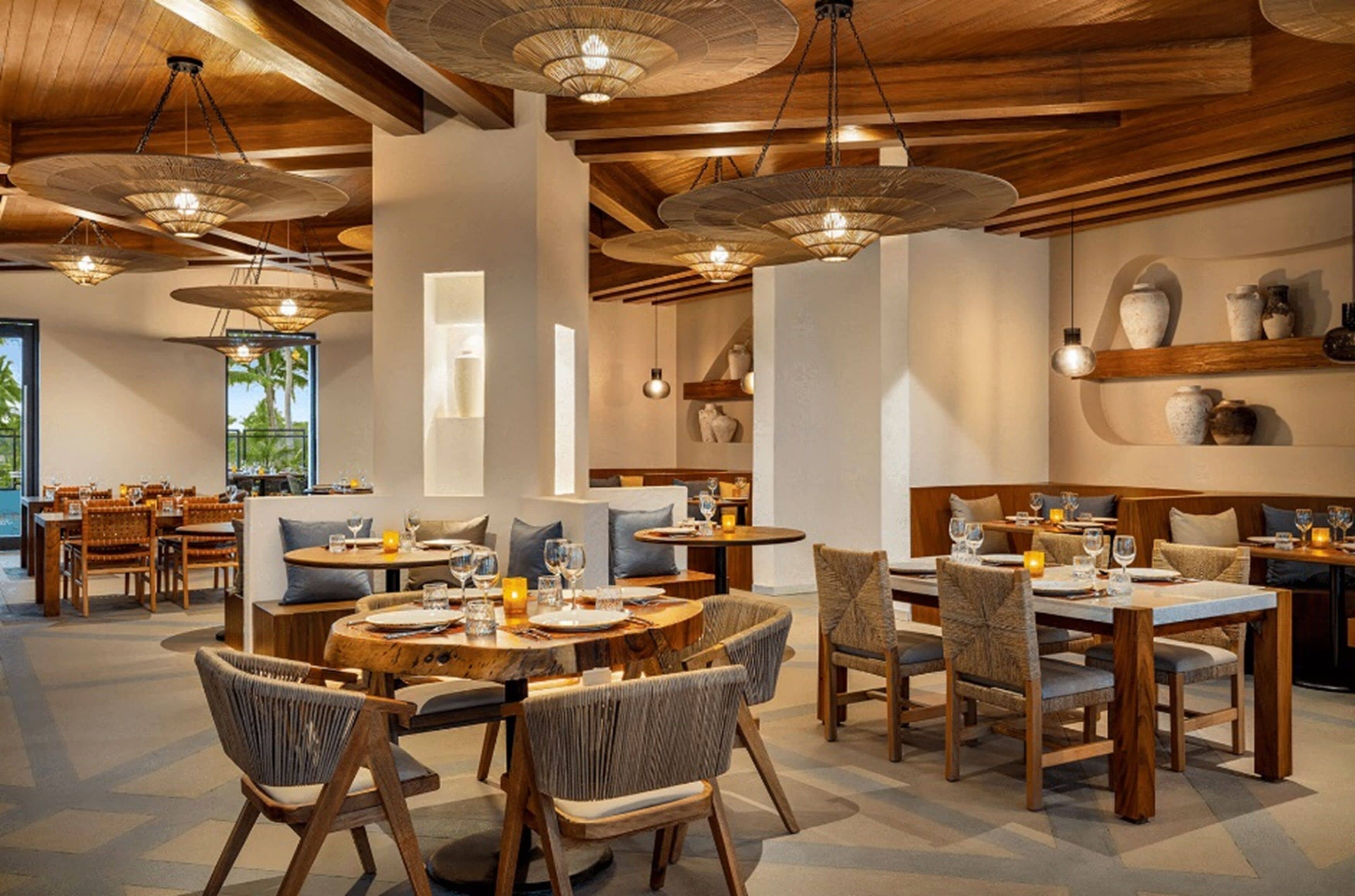A restaurant with round tables and chairs, wooden beams, and hanging light fixtures.