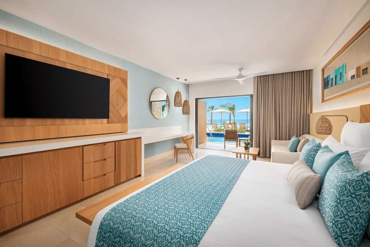 Une chambre d’hôtel moderne dotée d’un grand lit, d’une télévision à écran plat, d’un balcon avec vue sur la piscine et d’une armoire en bois.
