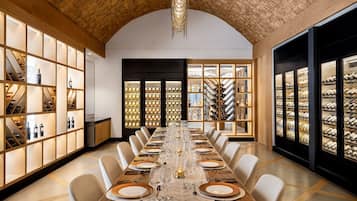 A long dining table set for a formal meal, flanked by wine racks and shelves with bottles.
