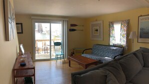 A living room with a sofa, a wooden coffee table, and a bench. There is a sliding glass door leading to an outdoor area with a patio table and chairs. - Huge Beach House with 2 car garage (Hampton)