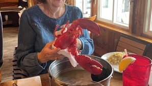 Une personne tenant un gros homard rouge à une table de restaurant, avec un bol de soupe, une assiette de riz et une boisson rouge.