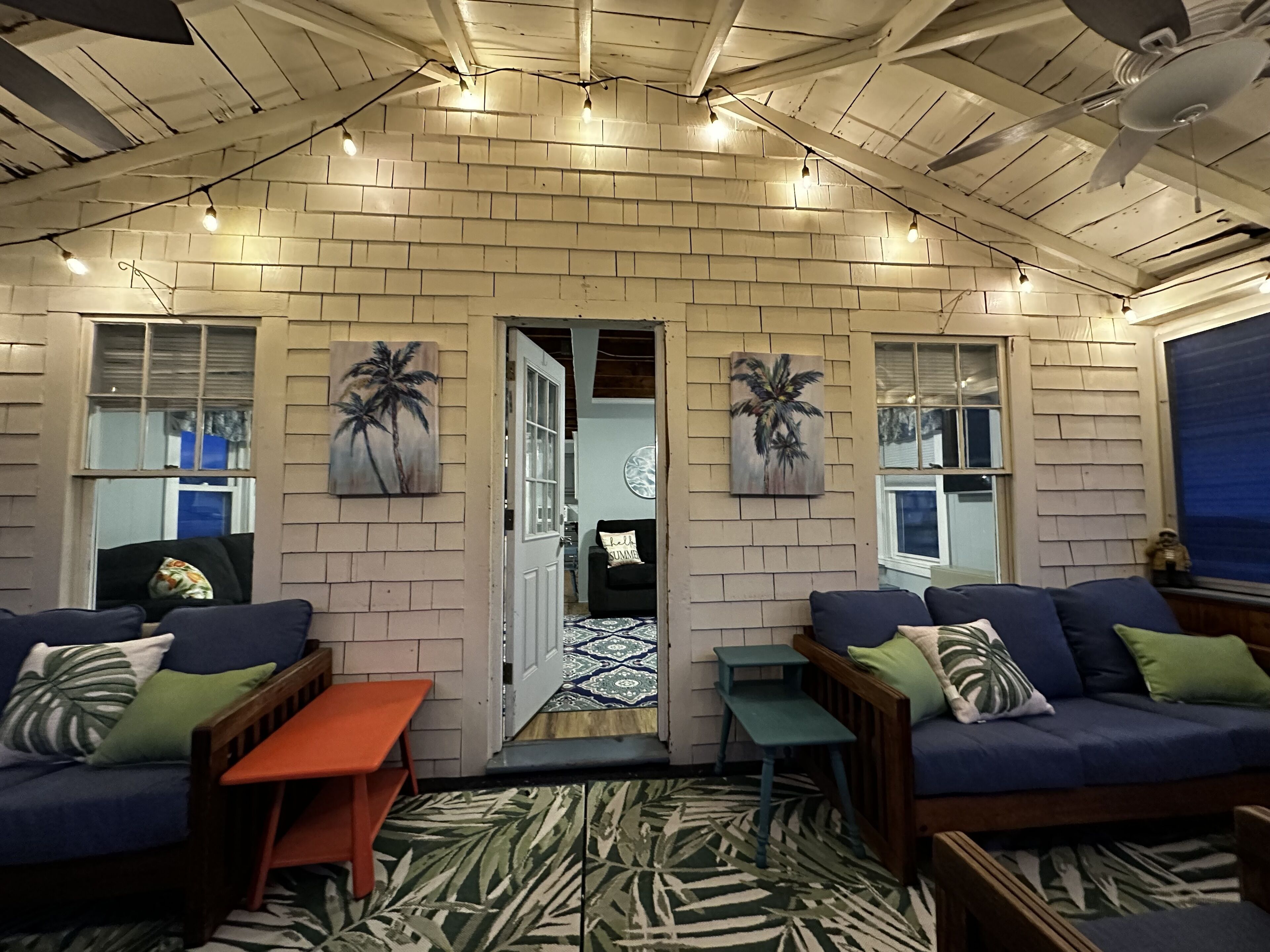 A cozy room with brick walls, two sofas, a small table, and palm tree artwork.
