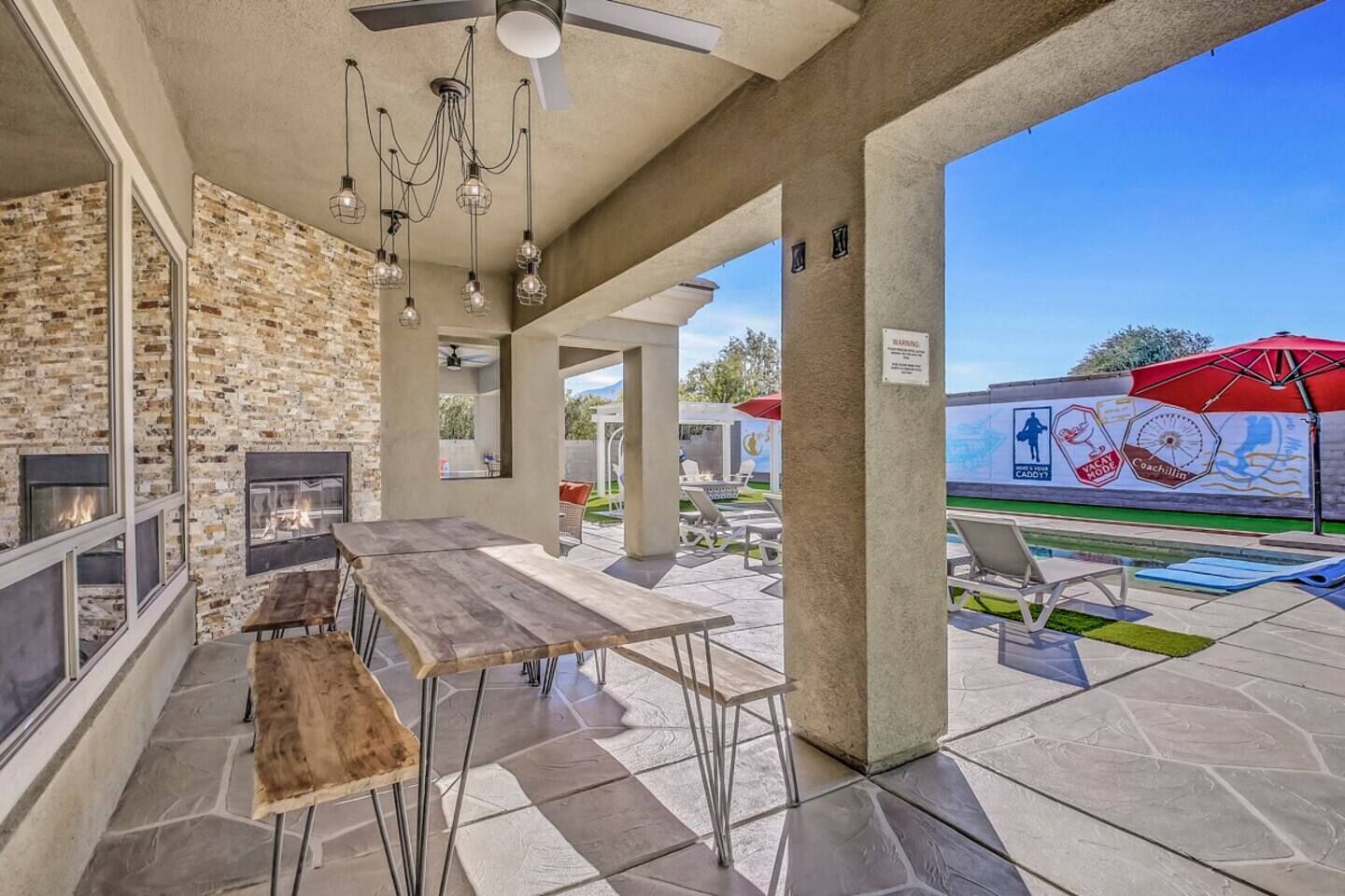 Une terrasse extérieure avec une cheminée en pierre, une table en bois et des fauteuils de jardin.
