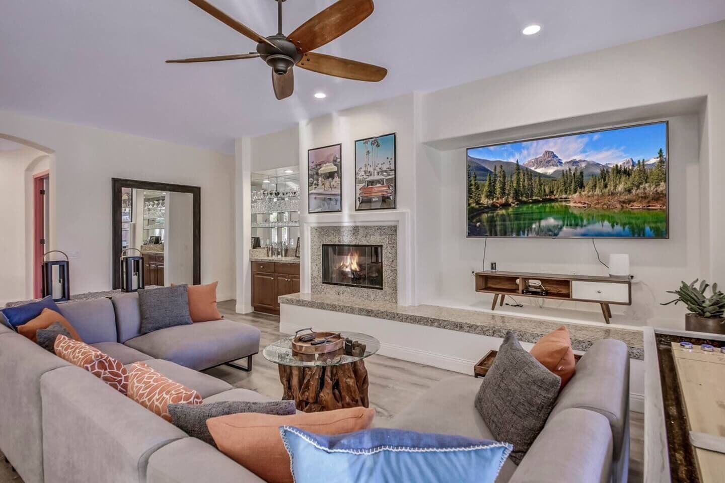 A modern living room with a large flat-screen TV, a fireplace, and a ceiling fan.
