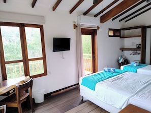 A room with a desk, two beds, a mounted TV, and an air conditioning unit.