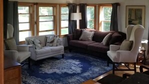 A living room with a ceiling fan, two sofas, a patterned rug, and large windows with curtains. - 3BR House Plus Bonus 1BR Apt at The Rockbound House 1Hr to Acadia National Park (Brooklin)