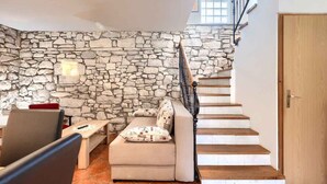 Un salon chaleureux avec un mur en pierre, un escalier en bois et un canapé agrémenté de coussins à motifs.