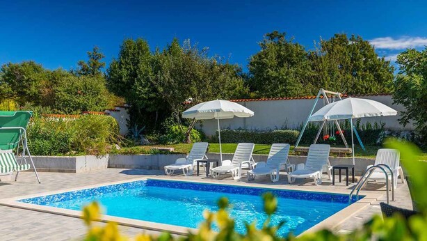 Une piscine entourée de verdure, avec des chaises longues et des parasols, sous un ciel dégagé.