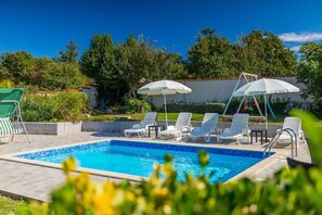 A swimming pool with lounge chairs and umbrellas, surrounded by greenery and a clear sky. - Villa with terrace, pool and air conditioning (Krnica)