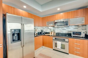 A modern kitchen with wooden cabinets, stainless steel appliances, and a tiled backsplash. - Luxe Resort Condo - 2 Mi to Daytona Beach! (Holly Hill)