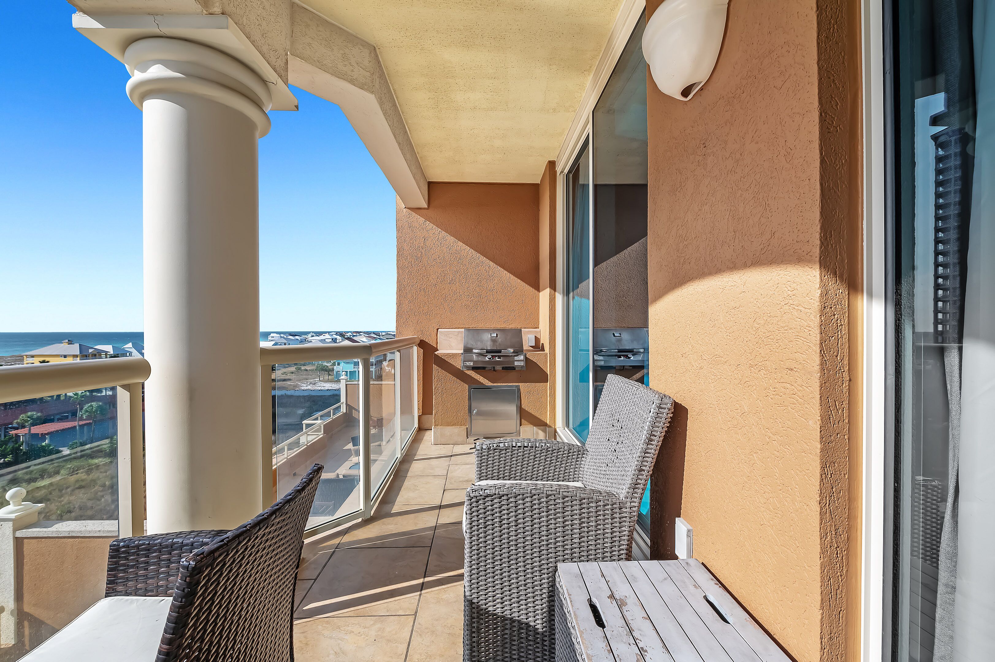 Een balkon met rieten meubilair, een barbecue en uitzicht over de stad.
