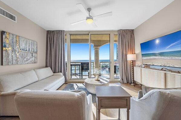 A hotel room with a balcony, a sofa, a coffee table, and a TV.