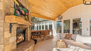 A stone fireplace with logs, a wooden ceiling, a white sofa, and a glass door leading outside.