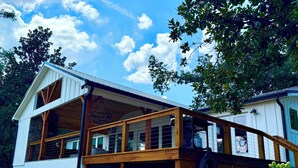 A wooden structure with a covered porch and large windows, surrounded by trees.