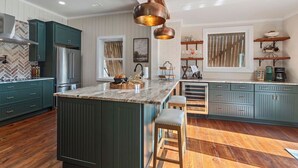 A kitchen with a central island, green cabinets, a herringbone-patterned backsplash, and pendant lighting.