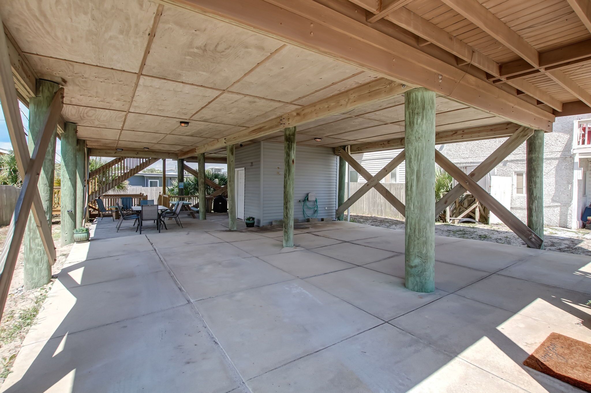 An open patio with a wooden deck, concrete flooring, and a view of a house in the background.