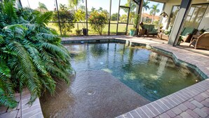 Une piscine bordée de briques, entourée d’une végétation luxuriante et de plantes en pot.