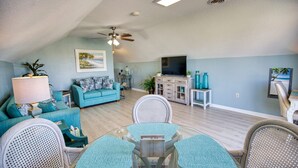 Un salon spacieux avec un canapé de couleur turquoise, une table à manger avec des chaises, un ventilateur de plafond et un téléviseur à écran plat.