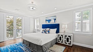Ein Schlafzimmer mit einem großen Bett, einem blauen Kopfteil, einem Gemälde darüber und Blick durch die Schiebetür.