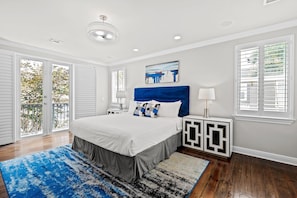 A bedroom with a large bed, a blue headboard, a painting above the bed, and a view through the sliding glass door.