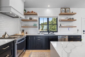 A modern kitchen with white subway tiles, black cabinets, stainless steel appliances, and wooden shelves. - Luxury Lakefront Home! Private Beach & Perfect for Entertaining! (Two Rivers)